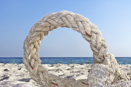 Old plaited artificial thick rope twisted into a ring lying on the seashoreの写真素材