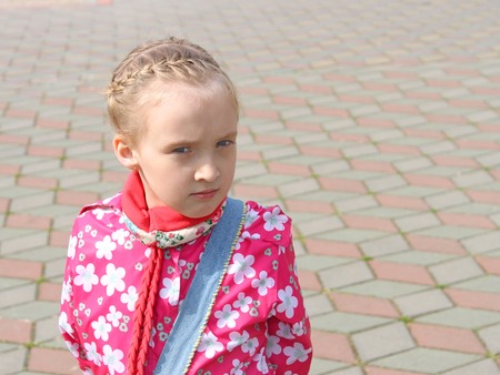 Portrait of small pensive Caucasian schoolgirl in a pink jacket on the square paved with colored tilesの写真素材