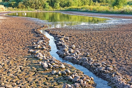 Water stream in artificially dug canal flows into the pond shrinkingの写真素材