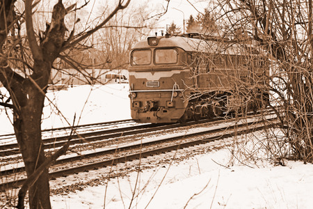 Single diesel locomotive moves across the railway tracks in wintertime, sepiaの写真素材