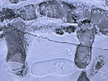 Frozen pond surface in winter with human prints and with cracked ice line, close-up