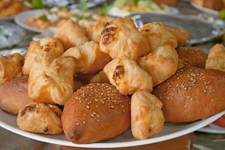 Buns with meat sprinkled with sesame seeds and other pastries on a plateの写真素材