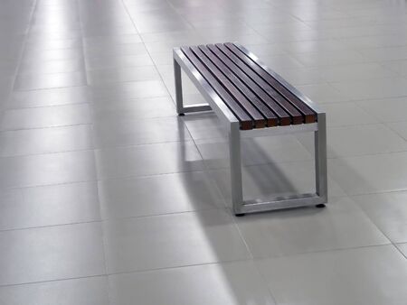 Bench with white metal steel frame and wooden seat elements on the grey tile floor and with cool lightingの写真素材