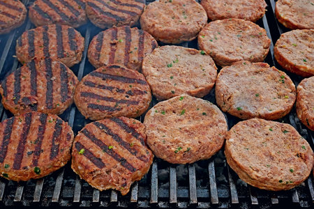 Meat cutlets of round shape fried on iron bars over hot charcoal, close-up