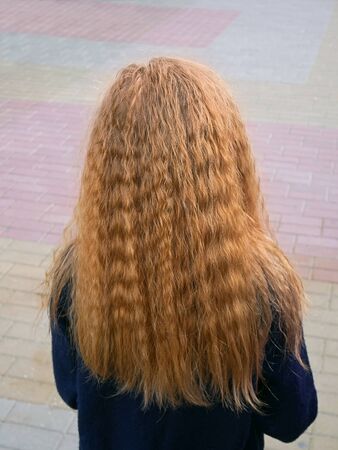 Little schoolgirl with long flowing wavy blond hair on the sidewalk of colored tiles, back viewの写真素材