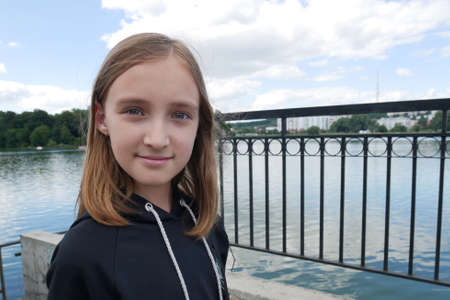 Teenage blond caucasian girl on the lake embankment in cloudy summer weatherの写真素材