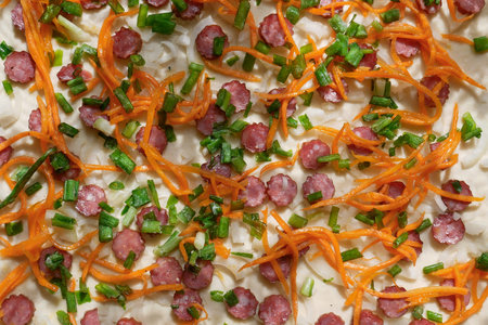 Detail of Pizza during the preparing for cooking with ingredients of sausages, long sliced carrot,...