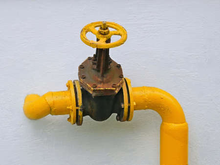 Old gas valve attached on the pipe that goes into the vertical house wallの写真素材