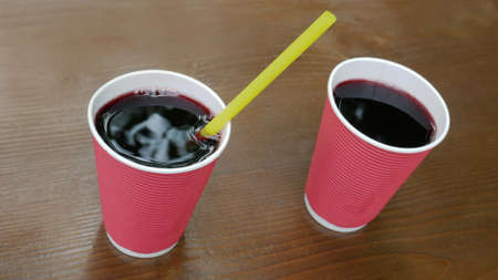 Two pink paper cups with a drink of dark red burgundy color standing on a lacquered wooden table, top view, close-upの写真素材