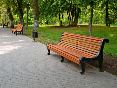 Empty alley with new benches and paved gray tiles in the city park in fine summer sunny day in Kyiv, Ukraineの写真素材