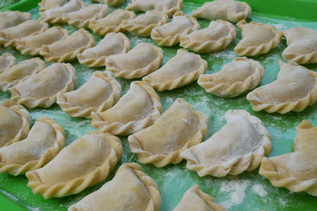Uncooked dumplings on a green kitchen tray with flour prepared and ready for cooking. Dumplings, or Varenyks with various fillings are traditional Ukrainian dishesの写真素材