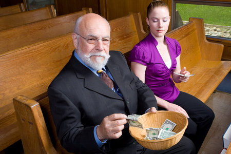 Senior man and young woman putting money into a church offering basket.  Looking at camera while...
