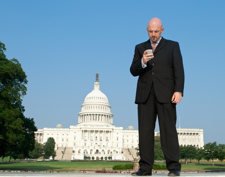 Businessman checking a smart phone in front of the U.S. Capital building in Washington, DC, United States.の写真素材