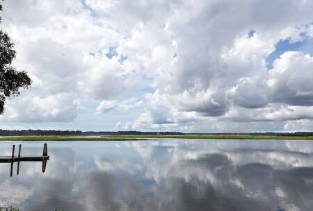 Dramatic Puffy White Clouds reflected in May River, Bluffton, South Carolina.  Dock on left.の写真素材