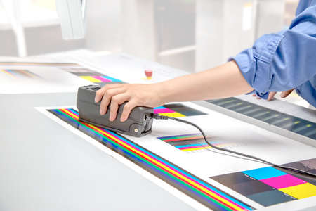 Close-up of the hand of colorimeter with a color watchtower against the background of a printing pressの写真素材