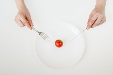 A mini tomato placed in the center of a plate is eaten with a knife and fork. Diet, rough eating,...