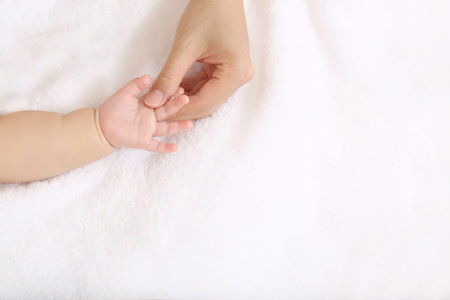 Mom's hand gently touching baby's hand on a white sheet