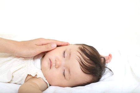 Mom's hand gently caressing the cheek of a baby girl sleeping on a white sheet