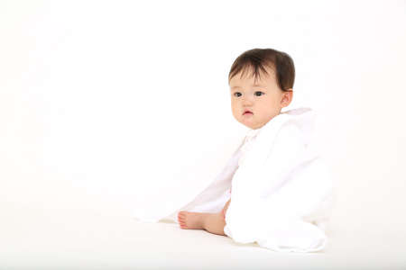 Baby girl sitting in front of a white background with a bath towelの写真素材