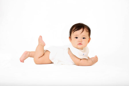 Baby girl in sideways figure with camera gaze high-high in front of a white backgroundの写真素材