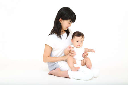 The whole body of a mother playing with baby girl in front of a white backgroundの写真素材