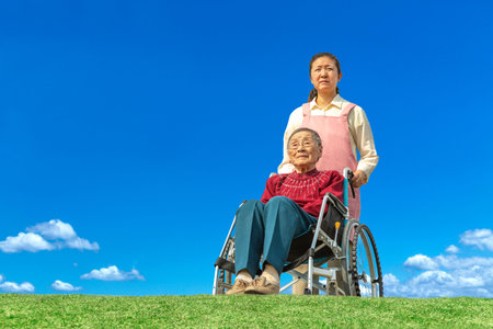A middle-aged woman cares for an elderly woman in a wheelchair against the backdrop of a blue sky