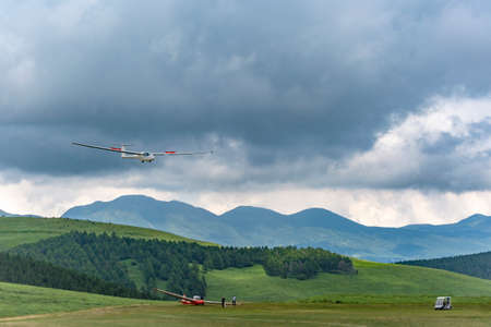 A glider landing on a high-altitude glide field against a backdrop of dark clouds and mountain ranges. Images of nature, the environment, and leisureの写真素材