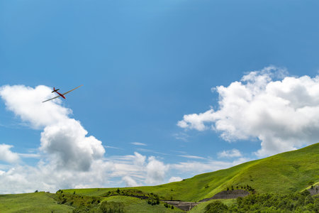 A glider flying down the green hills of the highlands against a backdrop of blue skies and white...