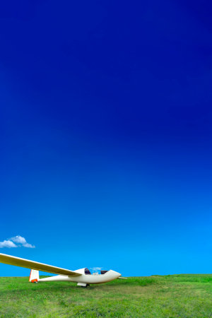 A white glider parked on a green plateau against a blue skyの写真素材
