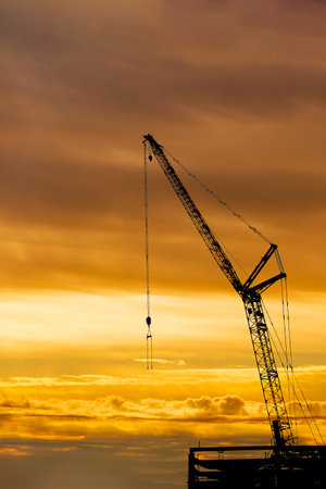 Silhouette of crawler crane arm towering high against sunset sky (background material)の写真素材