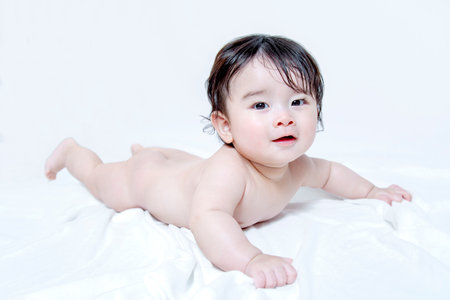Baby face down looking at camera face down in front of white backgroundの写真素材