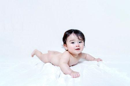Baby face down looking at camera face down in front of white backgroundの写真素材