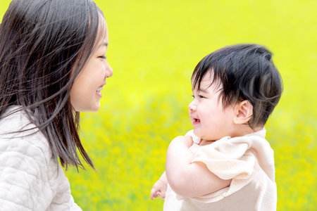 Baby playing with her sister in front of the rape flower field. Family, affection, friendship imageの写真素材