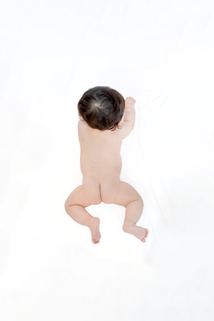 Overhead view of a baby lying face down  on white sheets from directly aboveの写真素材