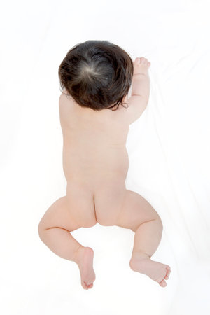 Overhead view of a baby lying face down  on white sheets from directly aboveの写真素材