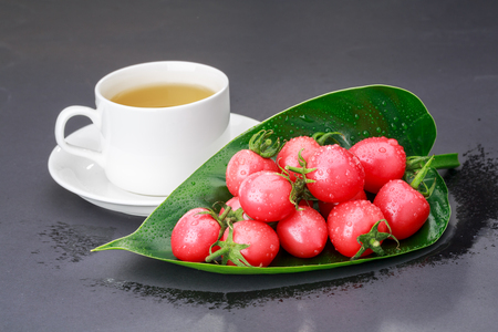 A cup of tea and small tomatoes on green leaf on black tableの写真素材