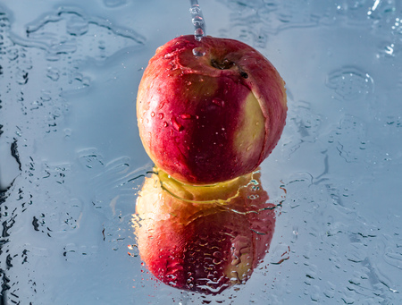 The process of washing one beautiful red apple with reflection and with splashes and drops of water on the mirror background we see in this photo.の写真素材