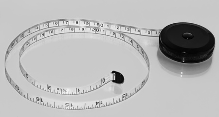 A black and white measuring tape for the waist measurement lies on a white glossy surface with reflectionの写真素材