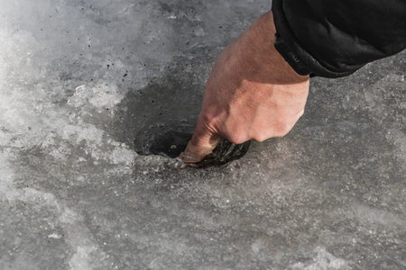 A man did a hole in the transparent white ice on a pond for winter fishing. A forefinger of a left...