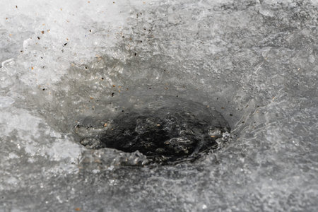 A hole in the transparent white ice is on a pond for winter fishingの写真素材