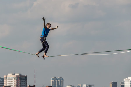 A man tightrope walker athlete extreme in blue pants and blue t-shirt walks over the city using...