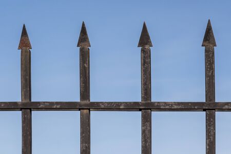The black shabby barbed metal fence is on a blue sky backgroundの写真素材