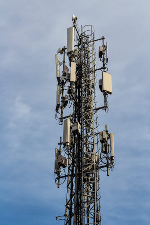 A gray metal cell tower carrying antennas of cellular networks on the blue sky with white clouds...