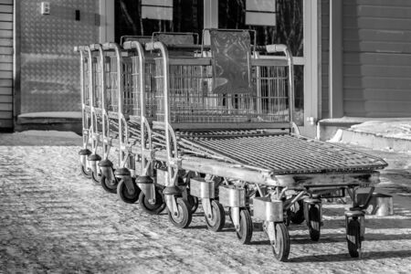 A large group of gray metal shopping storage baskets is outside in the snow in winter by the supermarketの写真素材