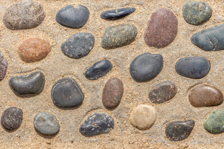 A beautiful texture of path of gray and color smooth stones on the yellow background with sand is in...