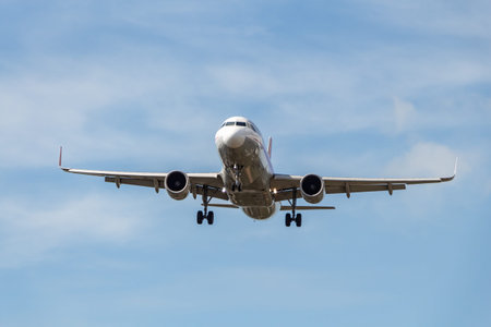 A white and silver plane with chassis is landing on the blue sky with clouds background