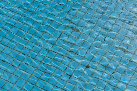 A beautiful texture of water with sun lights in a pool on the blue background of texture of small square ceramic tileの写真素材