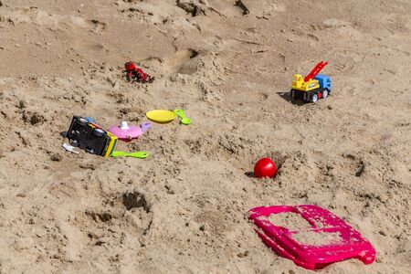 A beautiful yellow sandy beach with traces and footprints and a group of different colored children toysの写真素材