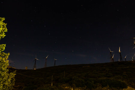 A group of white wind generators produces alternative energy by wind is on a black night sky with...