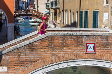 Venice / Italy - 08 08 2017: A woman in a red hat is on an old bridge over a canal in Venice in Italyのeditorial素材